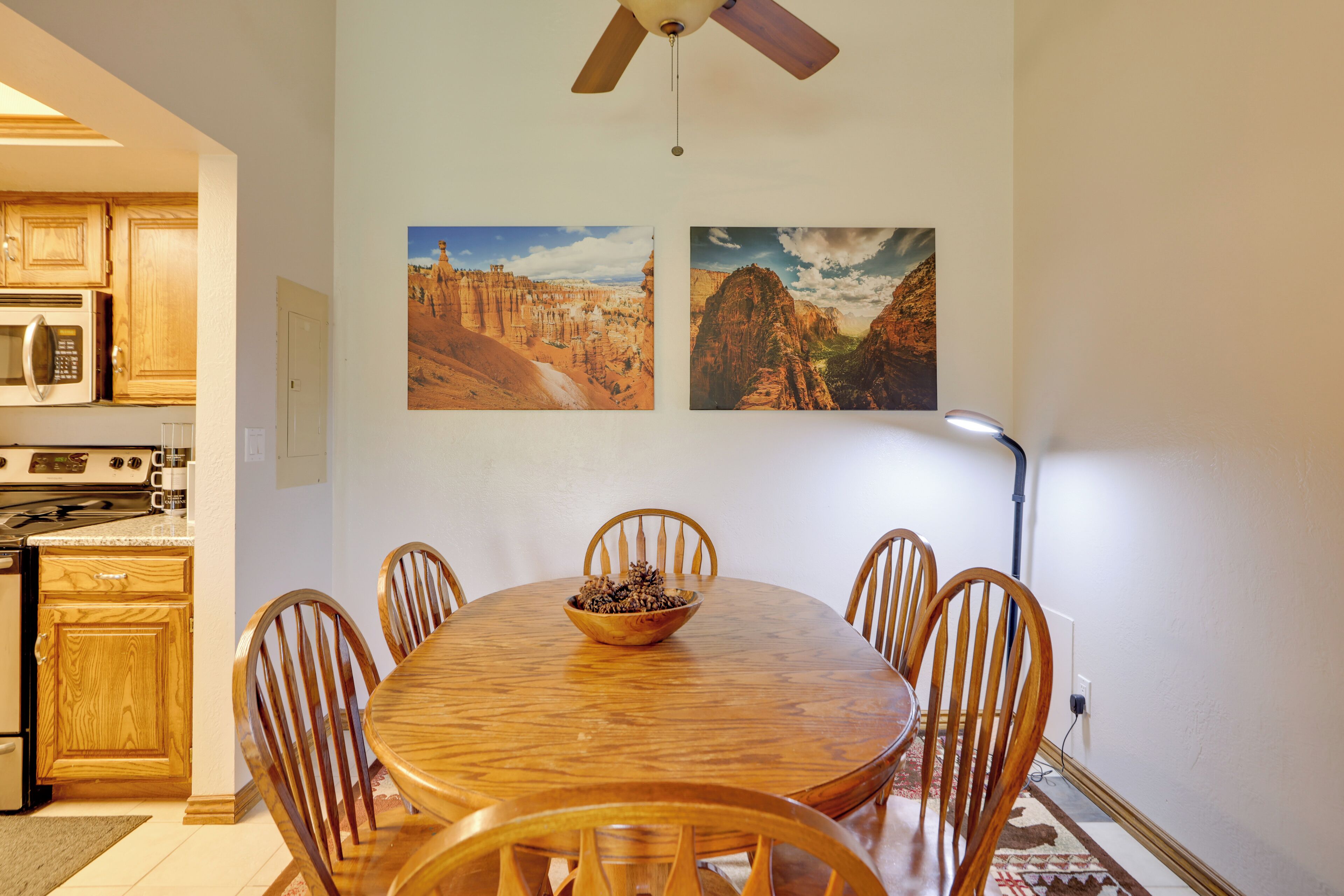 A dining area with a wooden table and chairs, a bowl of fruit, and two landscape paintings on the wall.