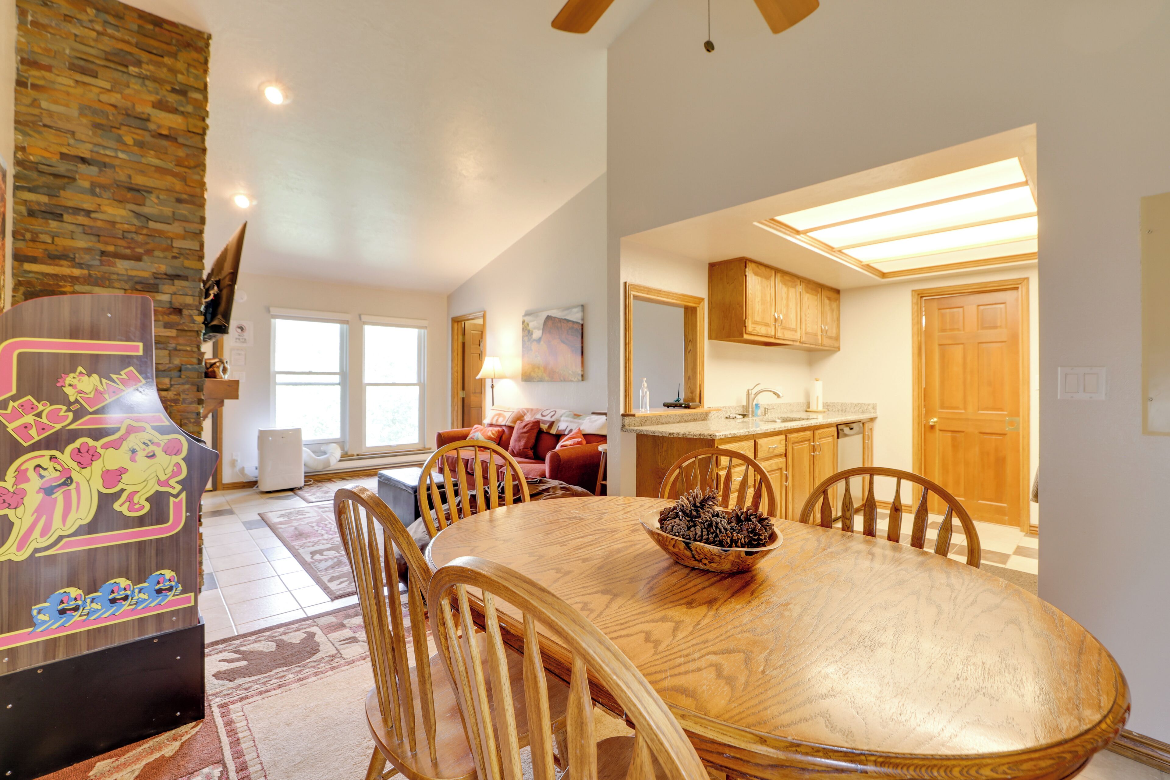 A spacious dining area with a large wooden table and chairs, a kitchen in the background, and a stone accent wall.