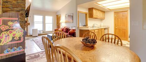 A spacious dining area with a large wooden table and chairs, a kitchen in the background, and a stone accent wall.