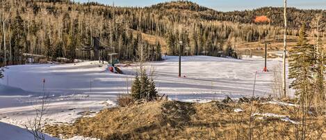 A snowy landscape with a ski lift and a forested hill in the background.