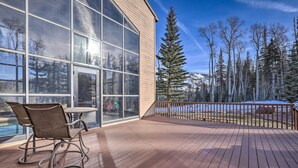 Eine Holzterrasse mit Glaswand, Gartenstühlen und Blick auf schneebedeckte Bäume.