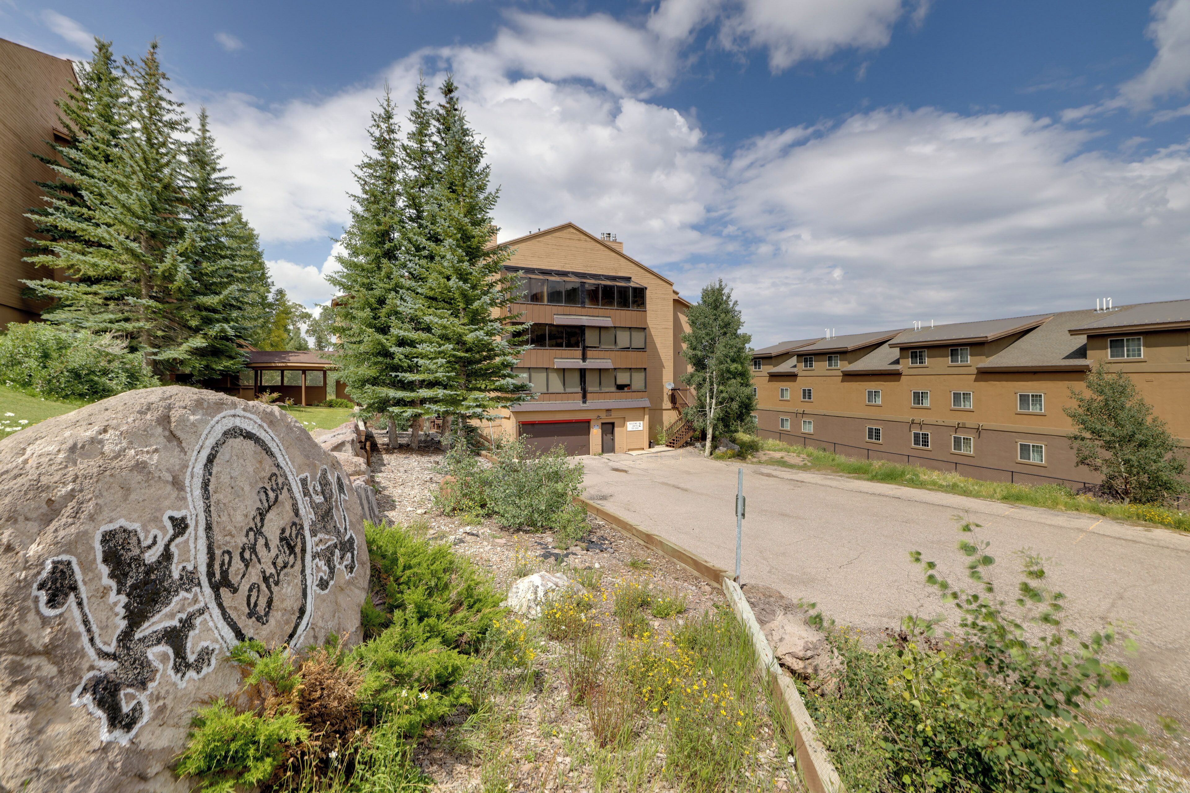 A multi-story building with a parking area, surrounded by trees and a large rock with text.