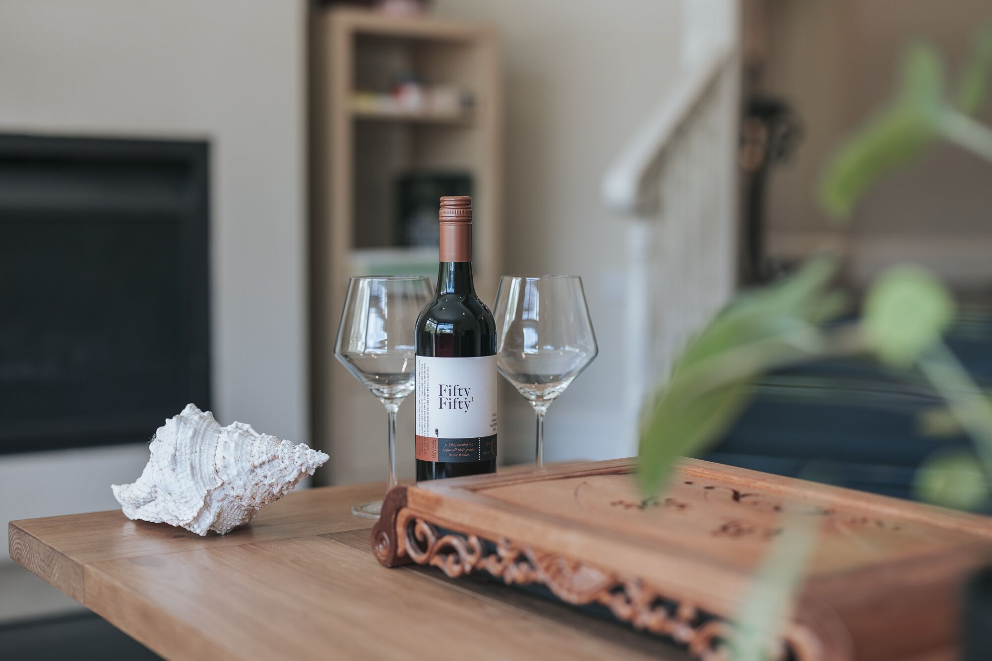 Une bouteille de vin sur une table en bois, accompagnée de deux verres, d’un morceau de tissu blanc et d’un plateau décoratif.