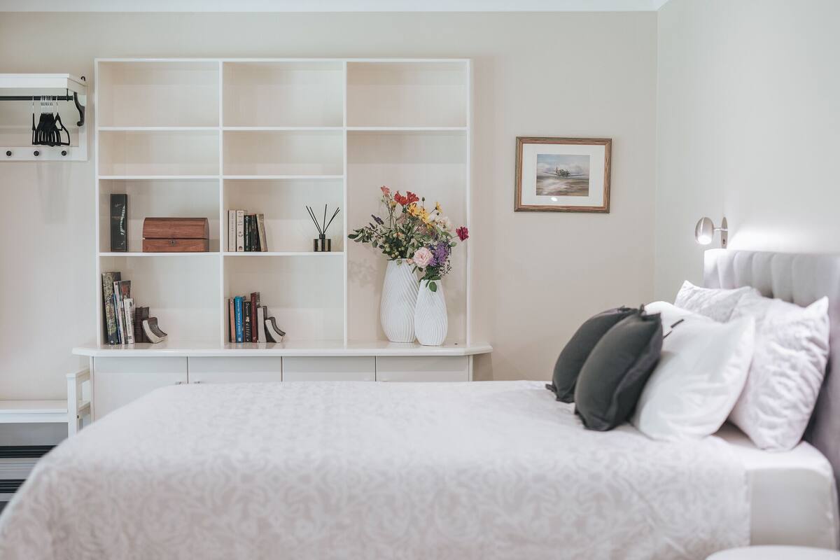 A bedroom with a large bed, a white wardrobe, and a small table with a vase of flowers.