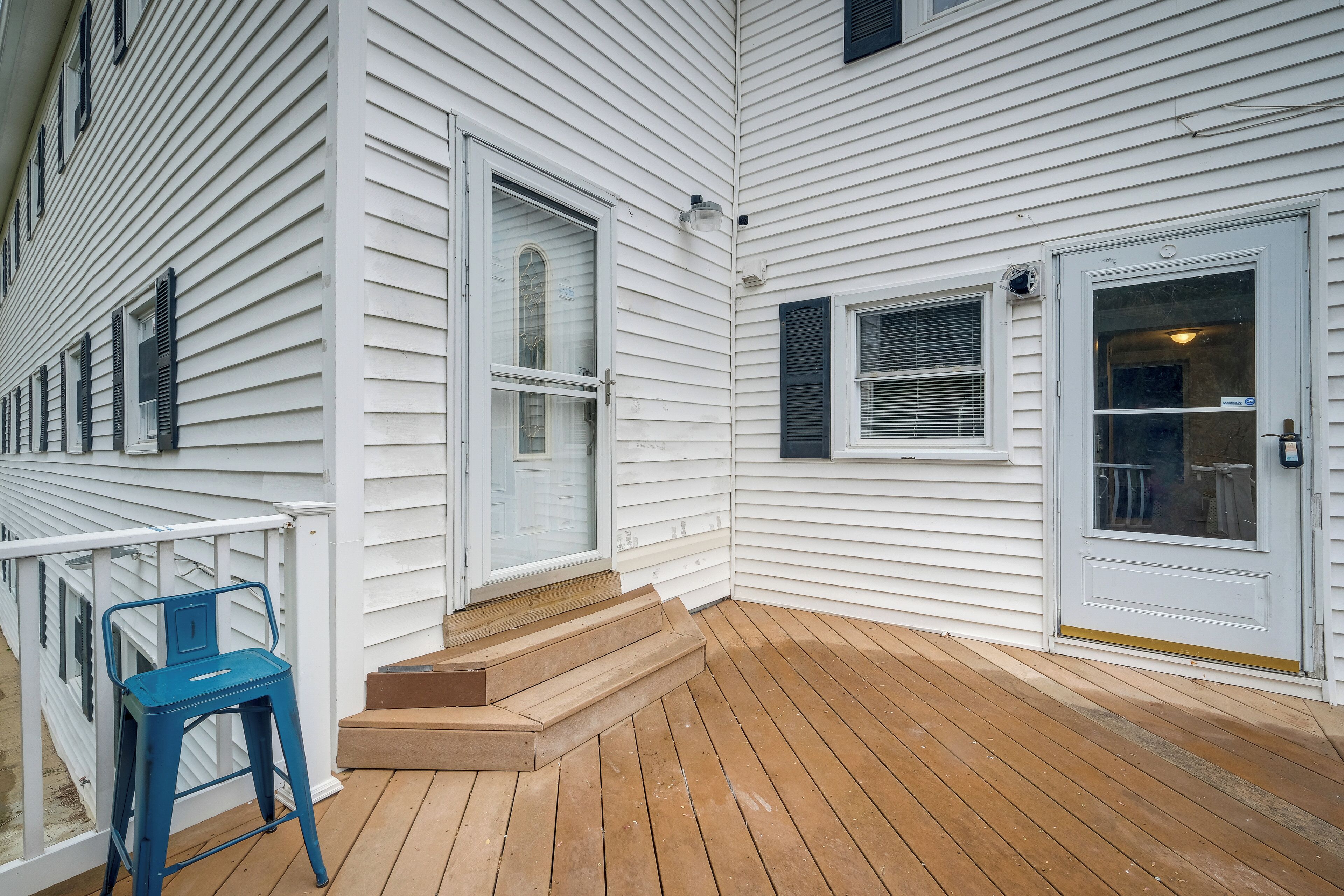 A wooden deck with steps leading to a white house with multiple windows and doors.