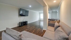 Ein großzügiges Wohnzimmer mit flachbildfernseher an der Wand, dunklem Holzboden und einem großen Ecksofa.