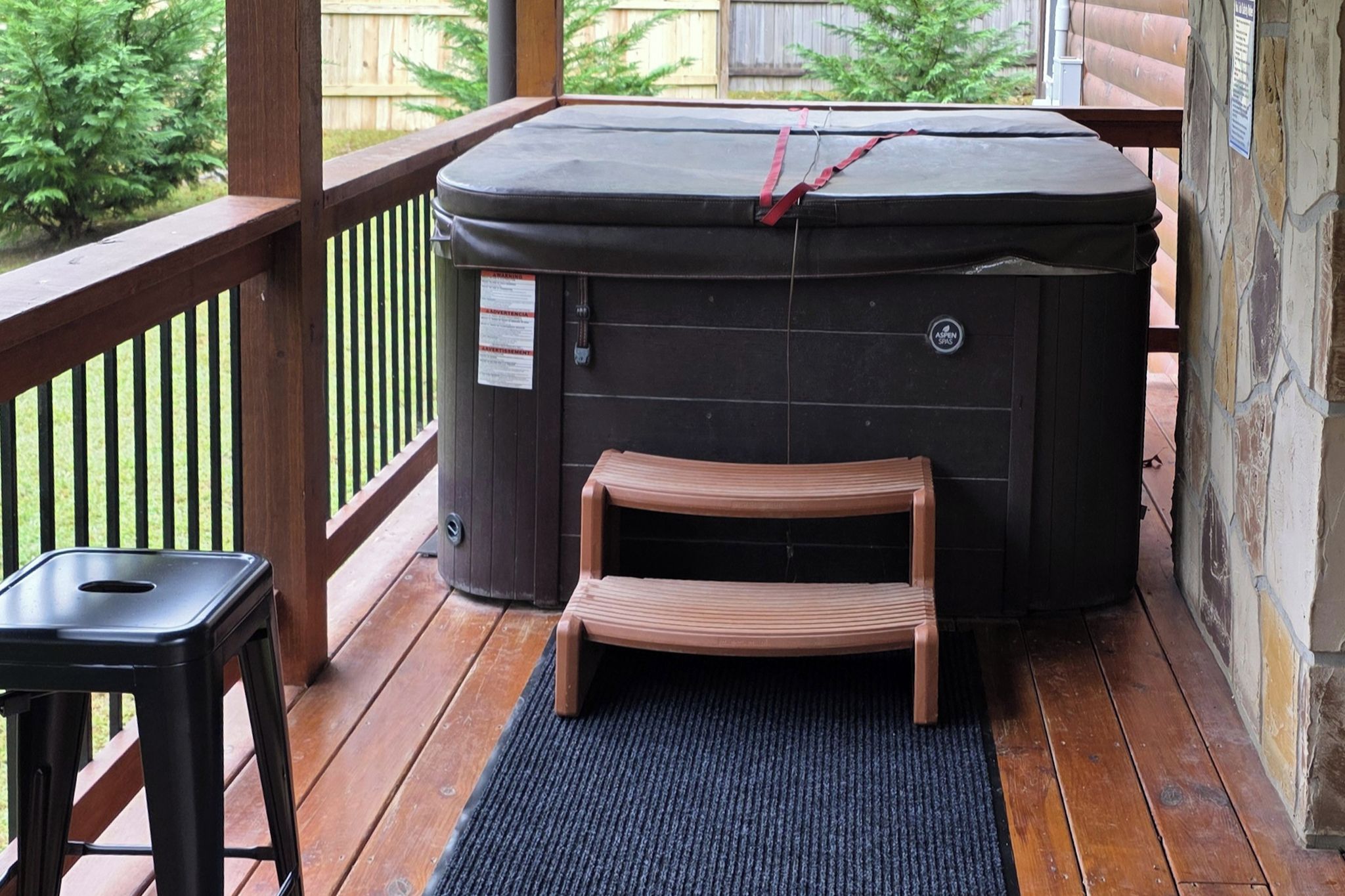 A hot tub on a wooden deck with a small wooden bench and a stool.