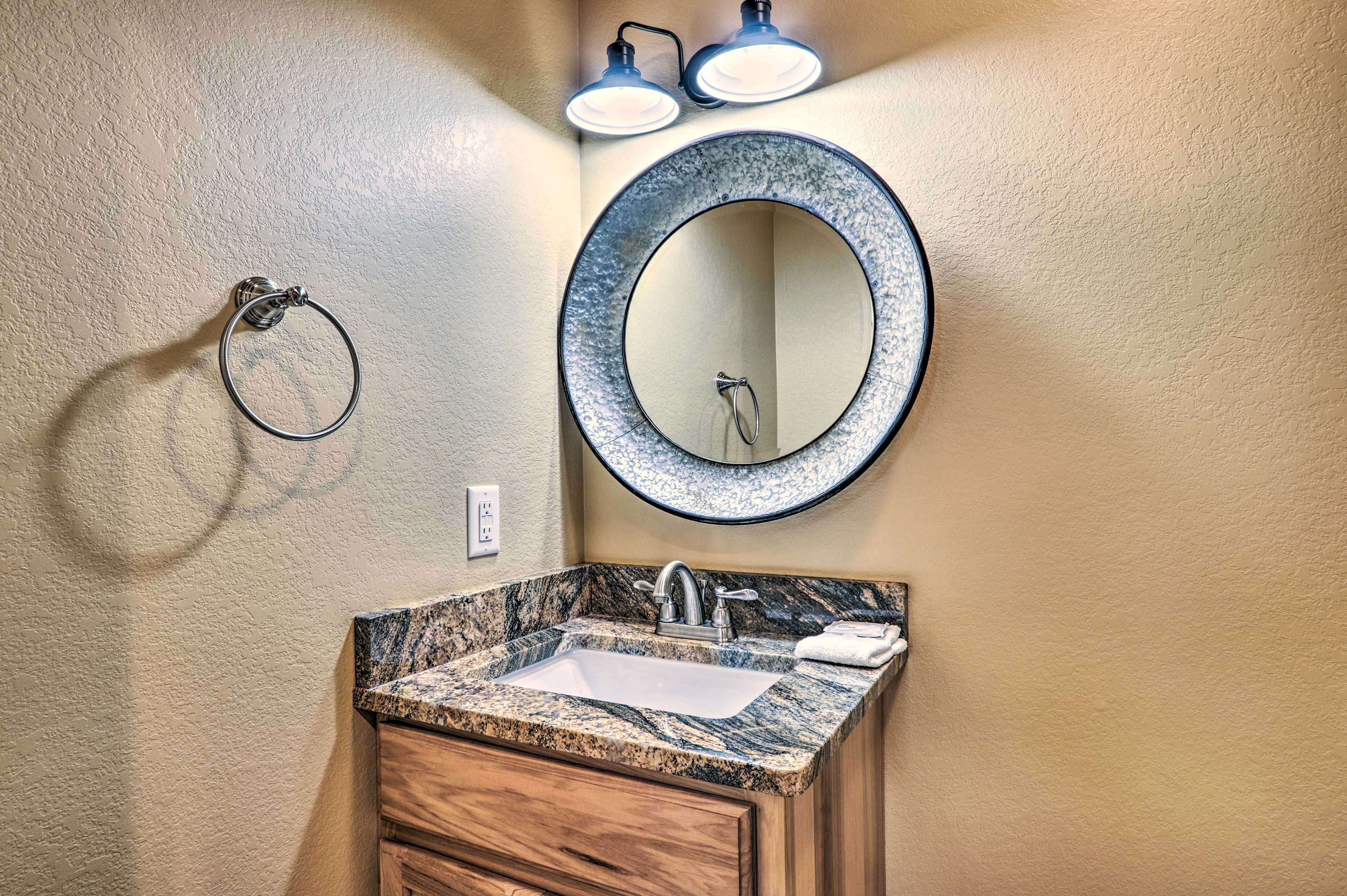 A bathroom with a granite countertop sink, a round mirror, and a towel rack.