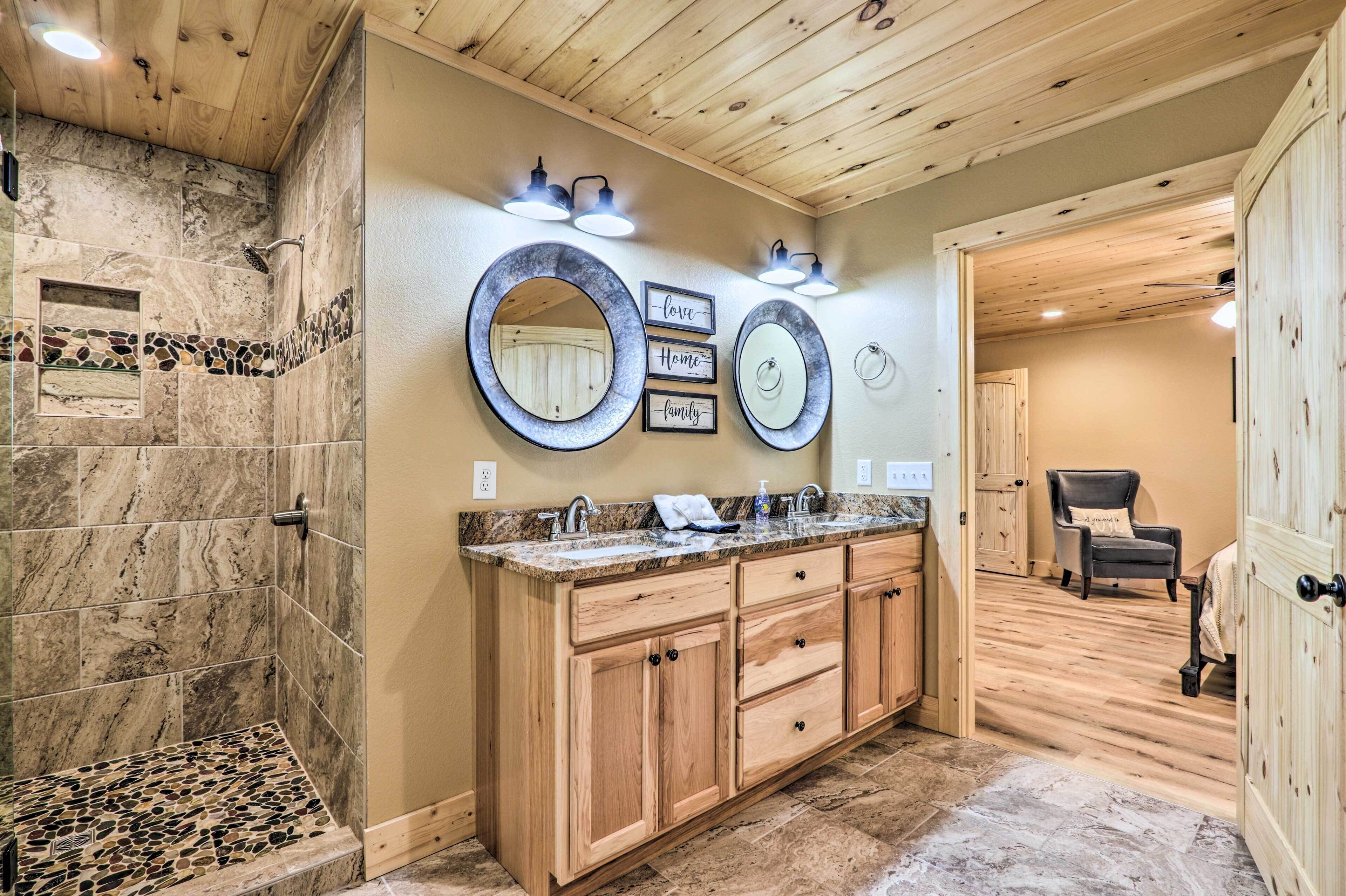 Een badkamer met een stenen douche, houten kastjes en een wastafel met twee spiegels.