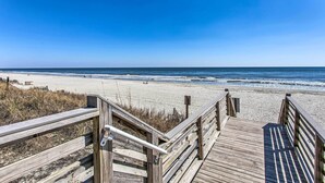 Een houten looppad dat naar een strand leidt, onder heldere luchten.