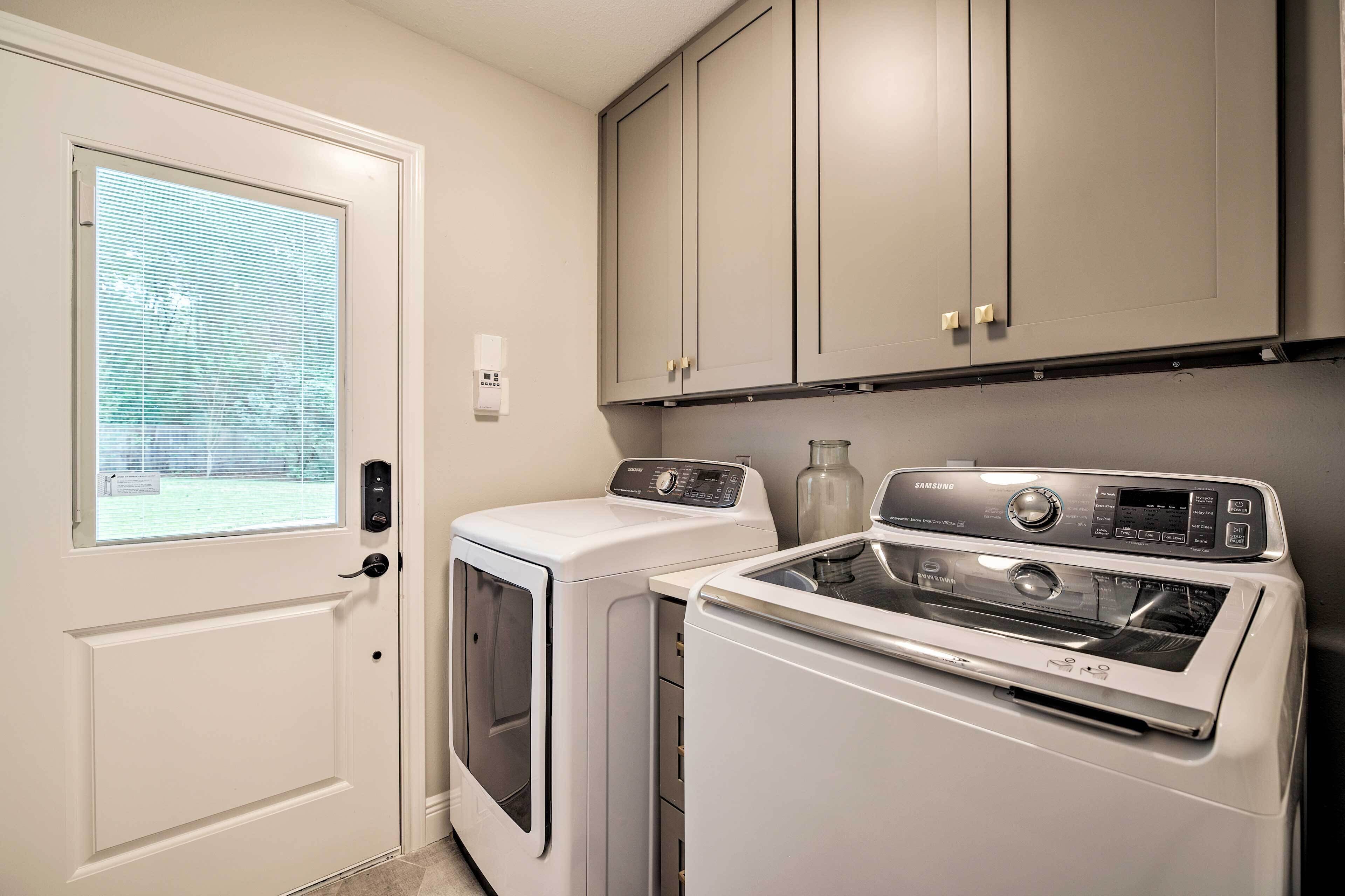 A laundry room with a front-loading washer and dryer, a window with blinds, and a door with a handle.