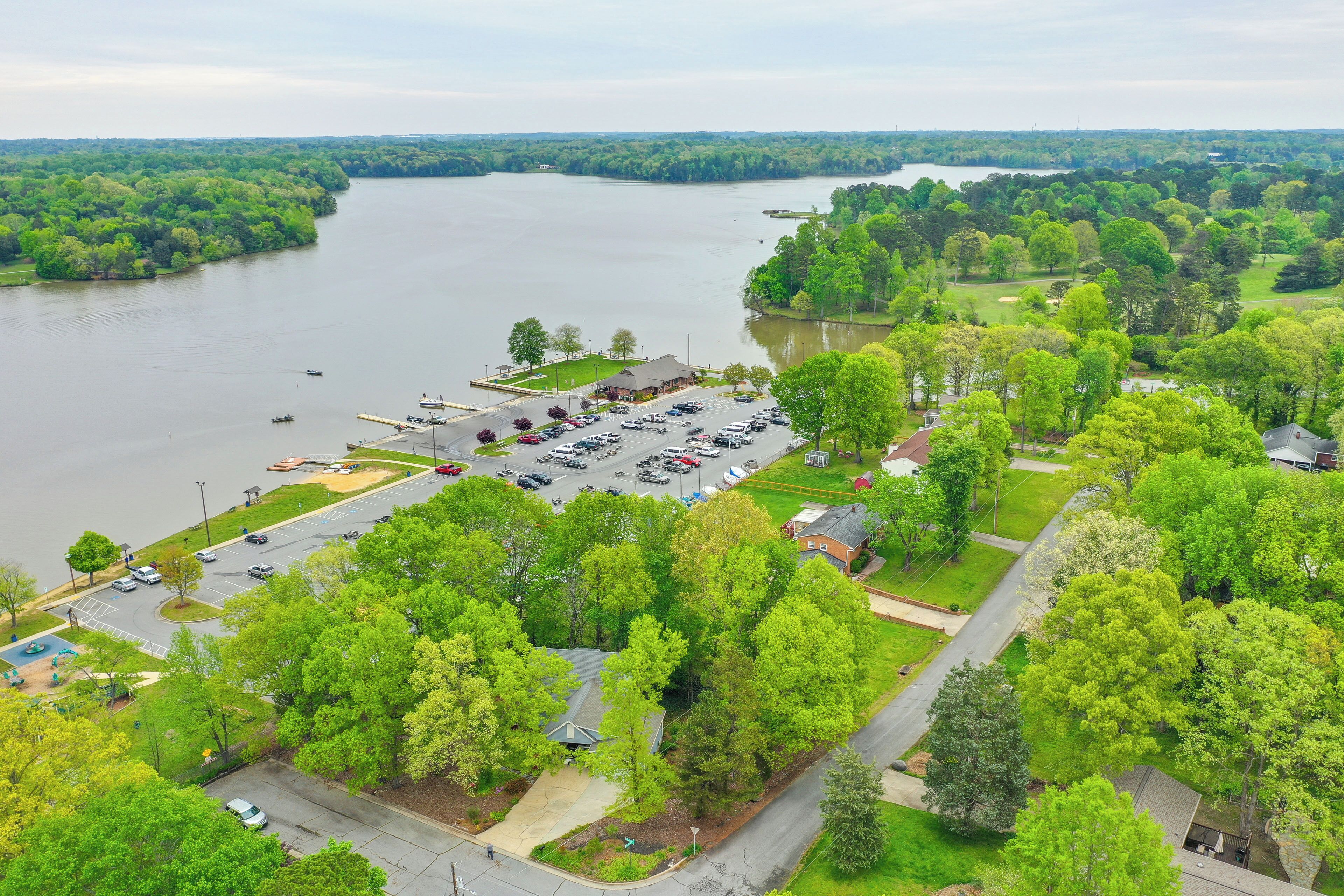 An aerial view of a lakeside property with a parking lot, a small building, and lush greenery.