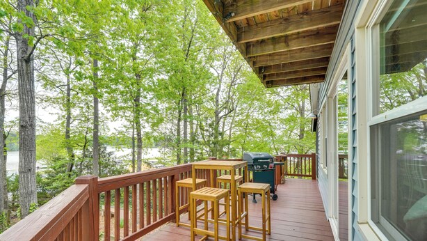 A wooden deck with outdoor furniture, a grill, and a view of a forested area.