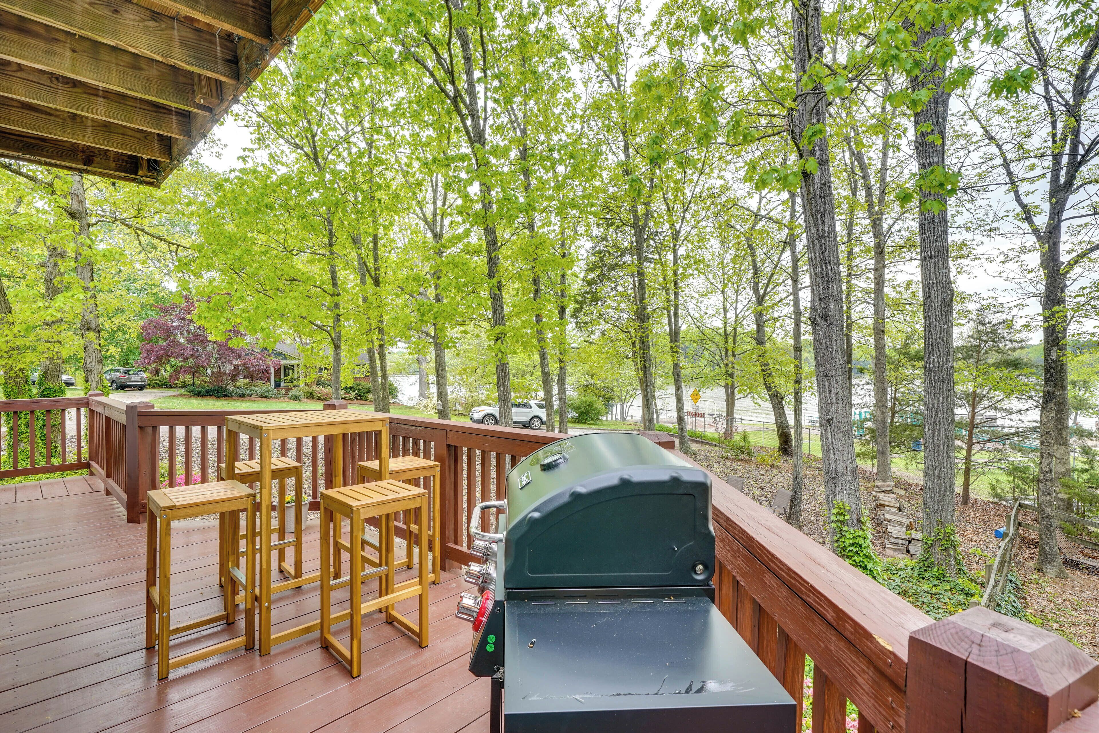Une terrasse en bois avec un barbecue et des tabourets de bar, donnant sur une zone boisée avec un lac.