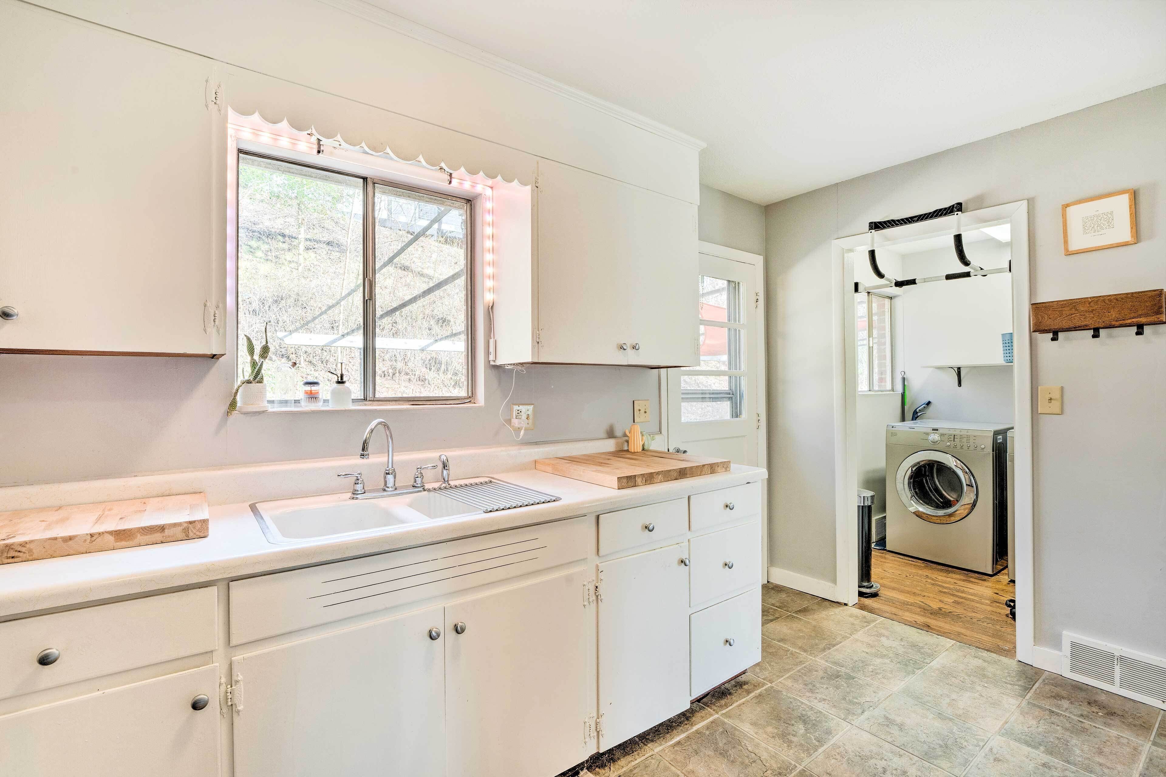 A kitchen with white cabinets, a sink, a wooden countertop, a window with a scalloped trim, and a washing machine in the adjacent room.