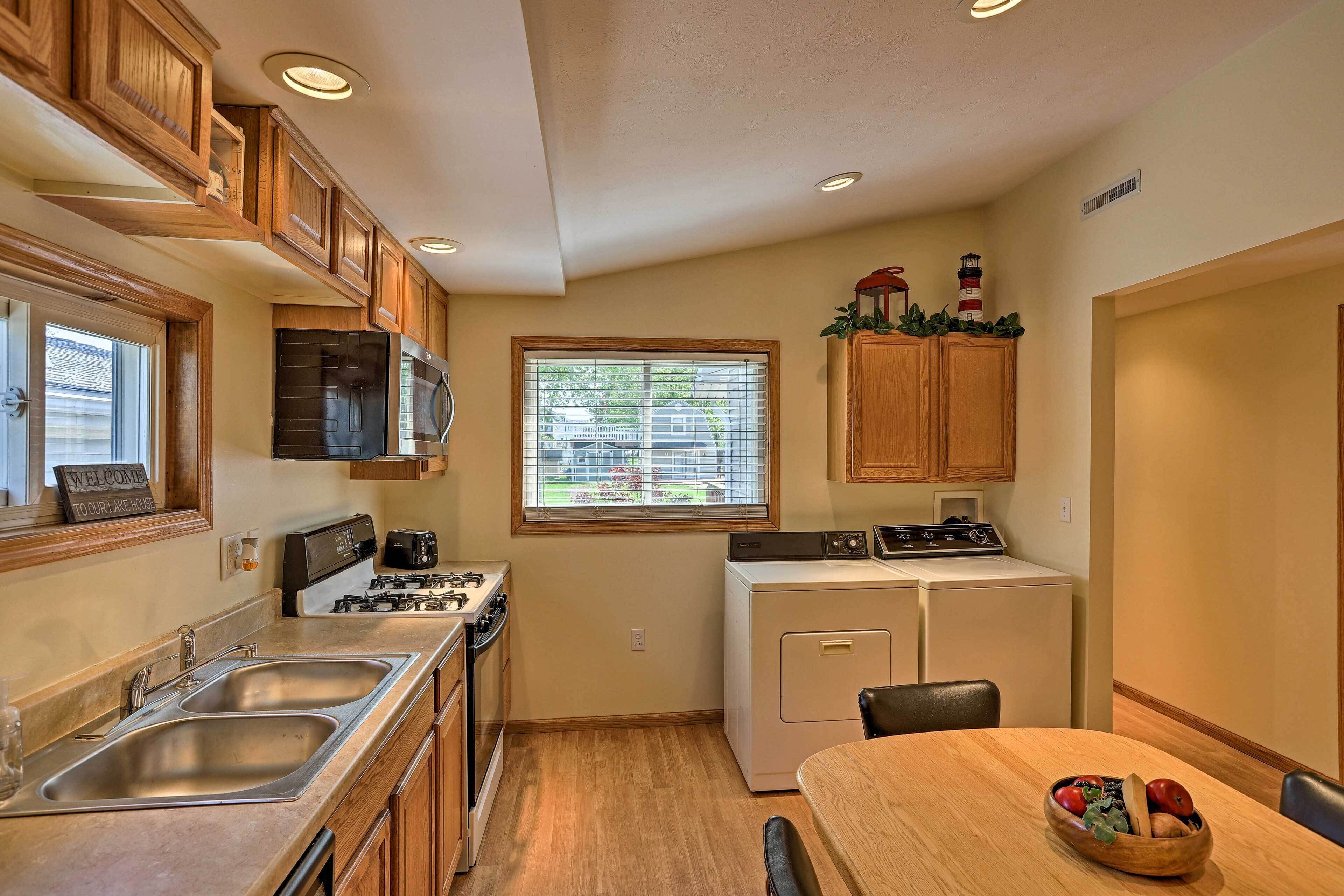 A compact kitchen with wooden cabinets, a built-in microwave, a stove, a sink, and a window with blinds.
