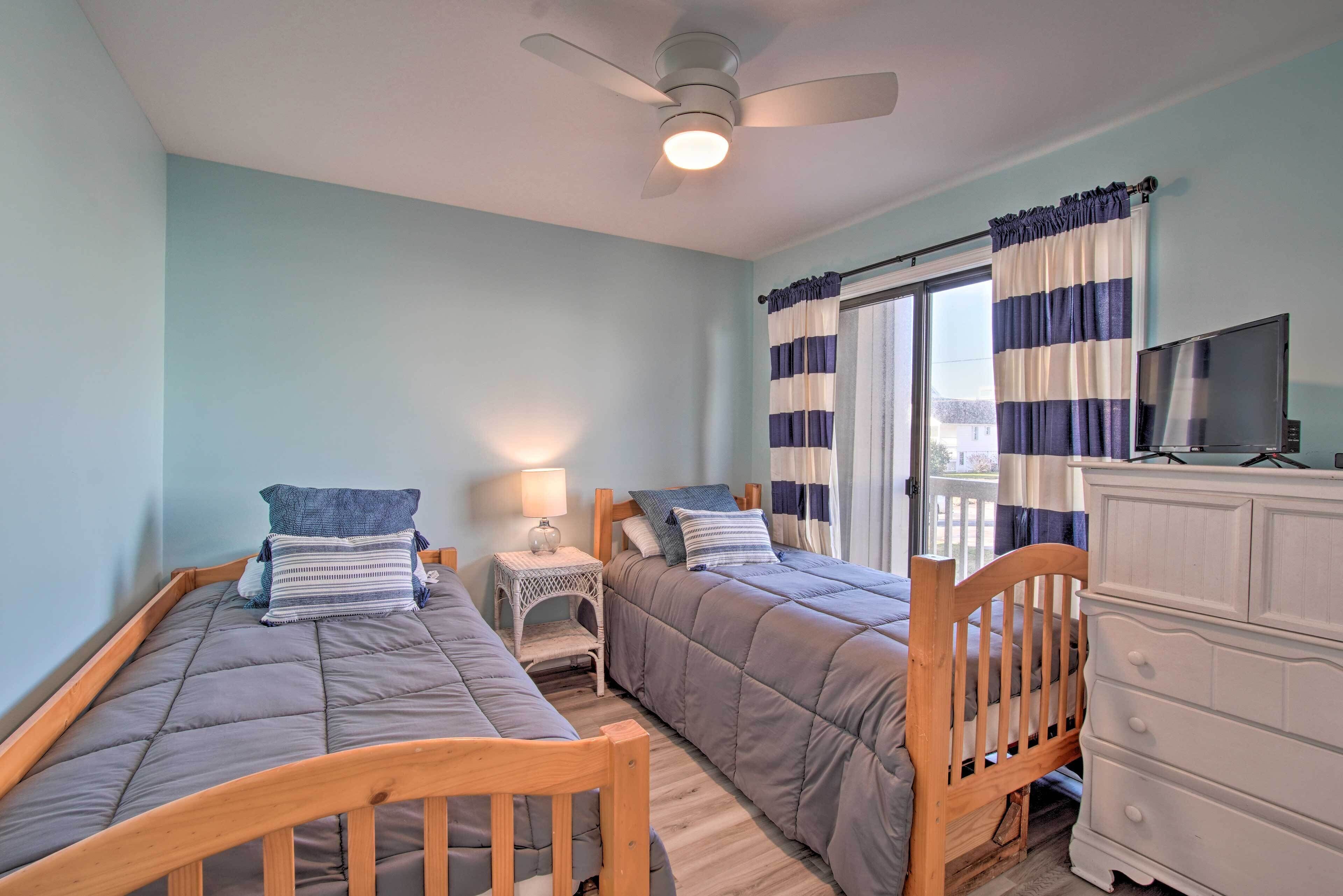 A bedroom with two single beds, a ceiling fan, a nightstand with a lamp, a dresser, and a TV.