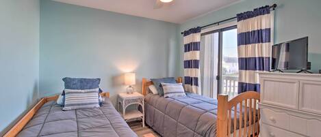 A bedroom with two single beds, a ceiling fan, a nightstand with a lamp, a dresser, and a TV.
