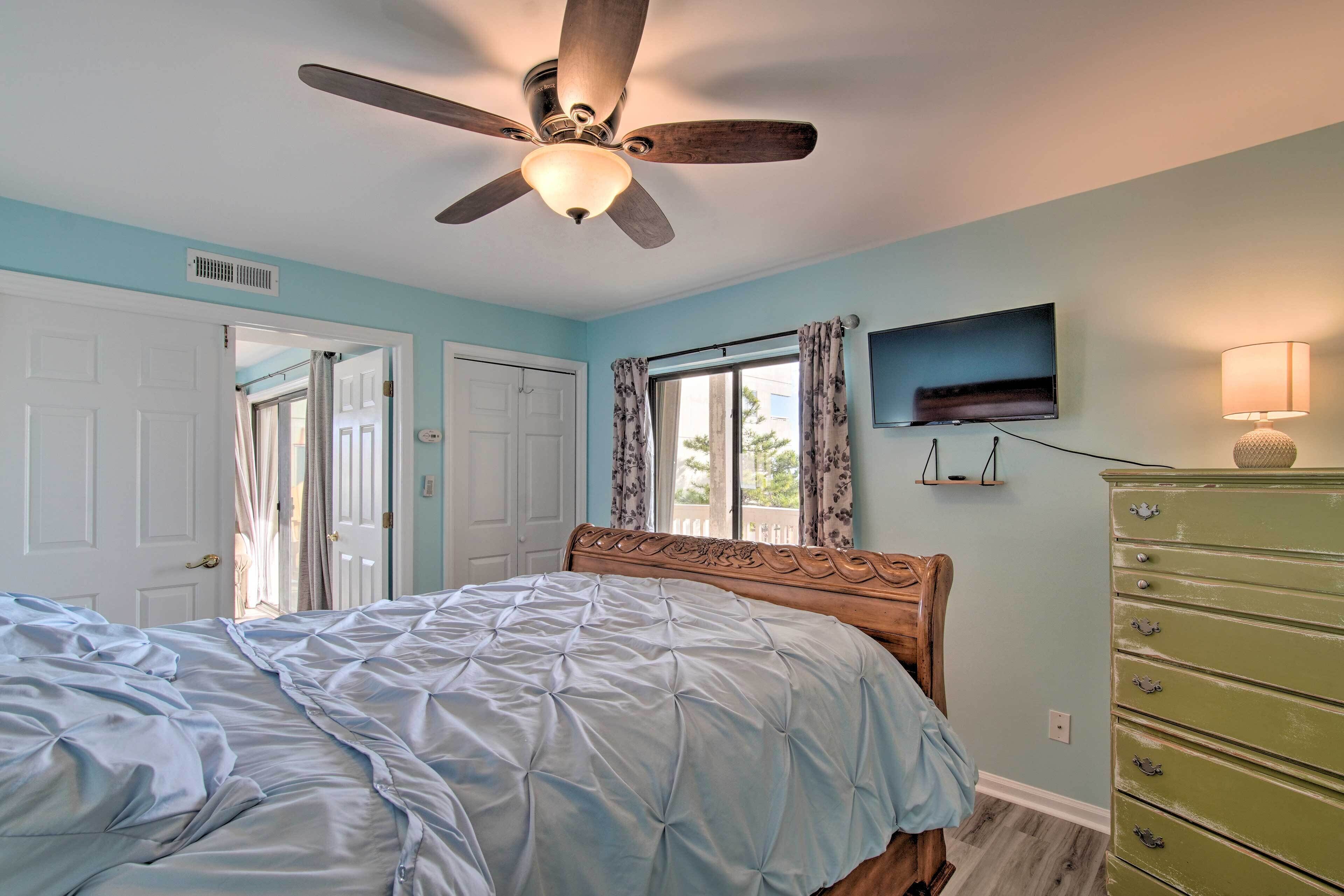 Une chambre avec un lit, un ventilateur de plafond, une commode et un téléviseur fixé au mur.