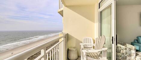 A balcony with a view of the ocean, white chairs, and a sofa with a floral pattern.