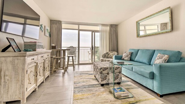A living room with a sofa, a coffee table, a cabinet, and a large window. - Oceanfront Resort Condo in North Myrtle Beach (North Myrtle Beach)