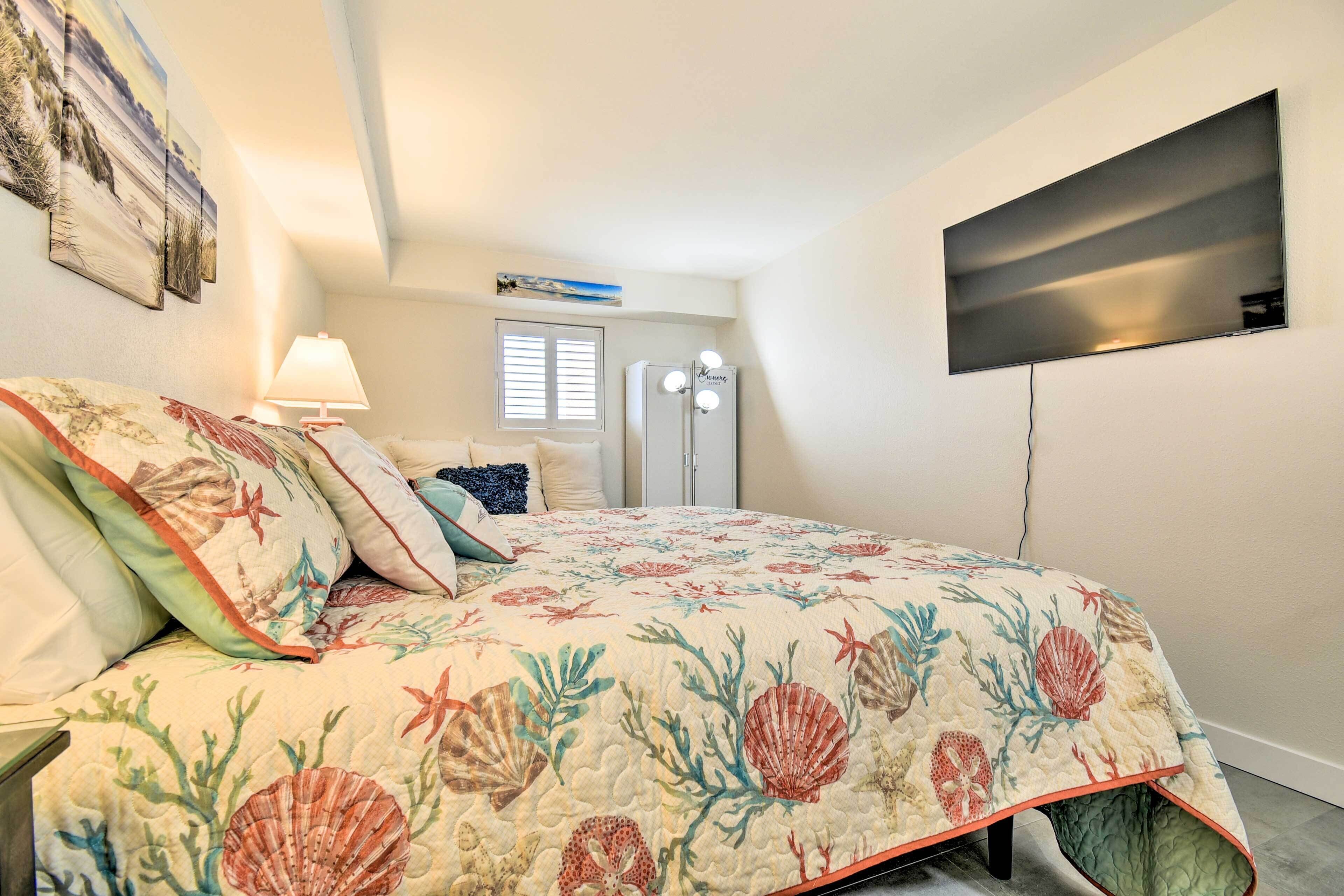 A bedroom with a bed, a nightstand, a lamp, a television mounted on the wall, and a window with blinds.
