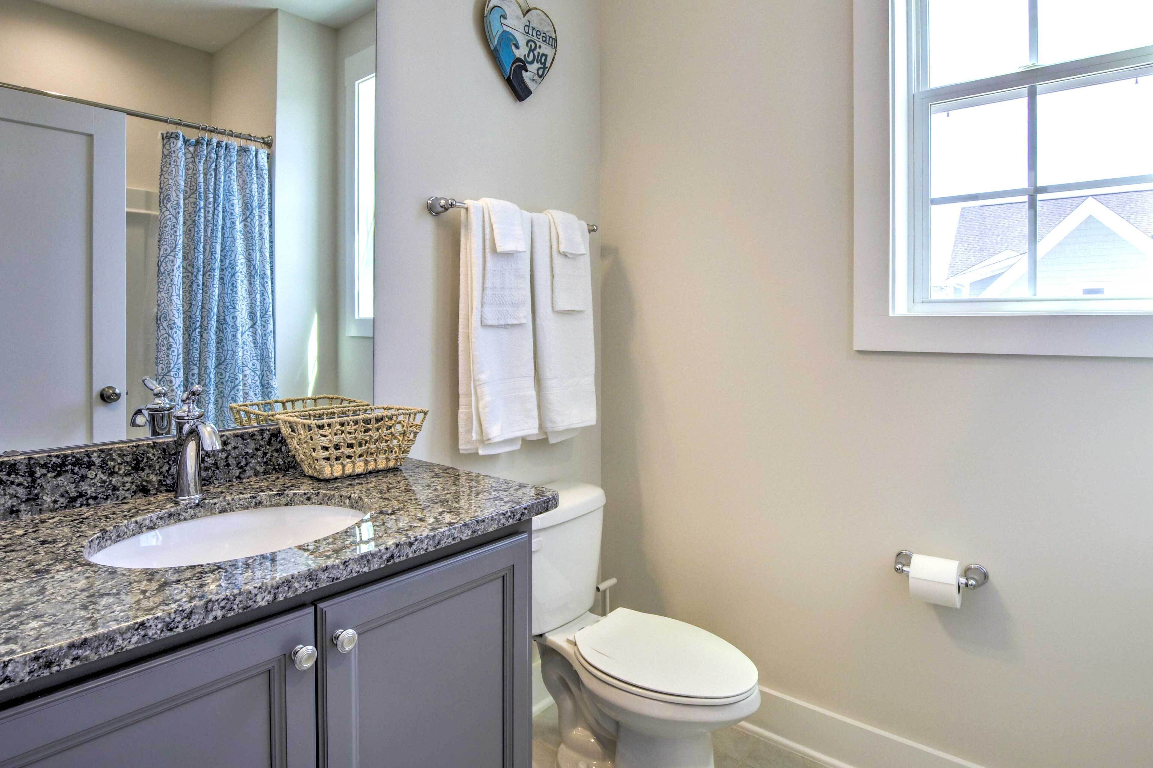 A bathroom with a granite countertop sink, a toilet, a basket, and a towel rack.
