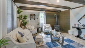 A cozy living room with a sofa, armchair, ottoman, and a coffee table. There is a fireplace, a bookshelf, and a potted plant.