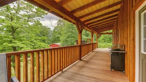 A wooden deck with a railing, a barbecue grill, and a view of trees and a red building in the background.