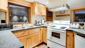 A kitchen with wooden cabinets, a stove, sink, and a window with blinds. - Ketchikan Apt - Walk to Refuge Cove Beach! (Ketchikan)