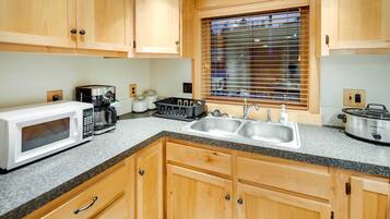 A kitchen with wooden cabinets, a microwave, a coffee maker, a toaster, a sink, and a window with blinds.
