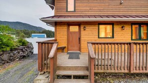A wooden cabin with a front door, a small porch, and a stone wall. - Ketchikan Apt - Walk to Refuge Cove Beach! (Ketchikan)