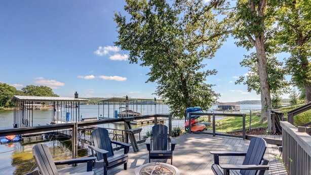 A deck with Adirondack chairs, a fire pit, and a view of a dock and water.