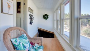 Una stanza con una sedia in vimini, pavimento in legno, un'asse decorativa a parete e vista su un corpo d'acqua attraverso ampie finestre.