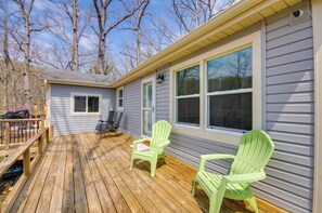 A deck with two green Adirondack chairs, a small table, and a wooden bench.