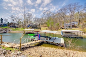 A lakeside property with docked boats, a covered boat launch, and residential buildings in the background.