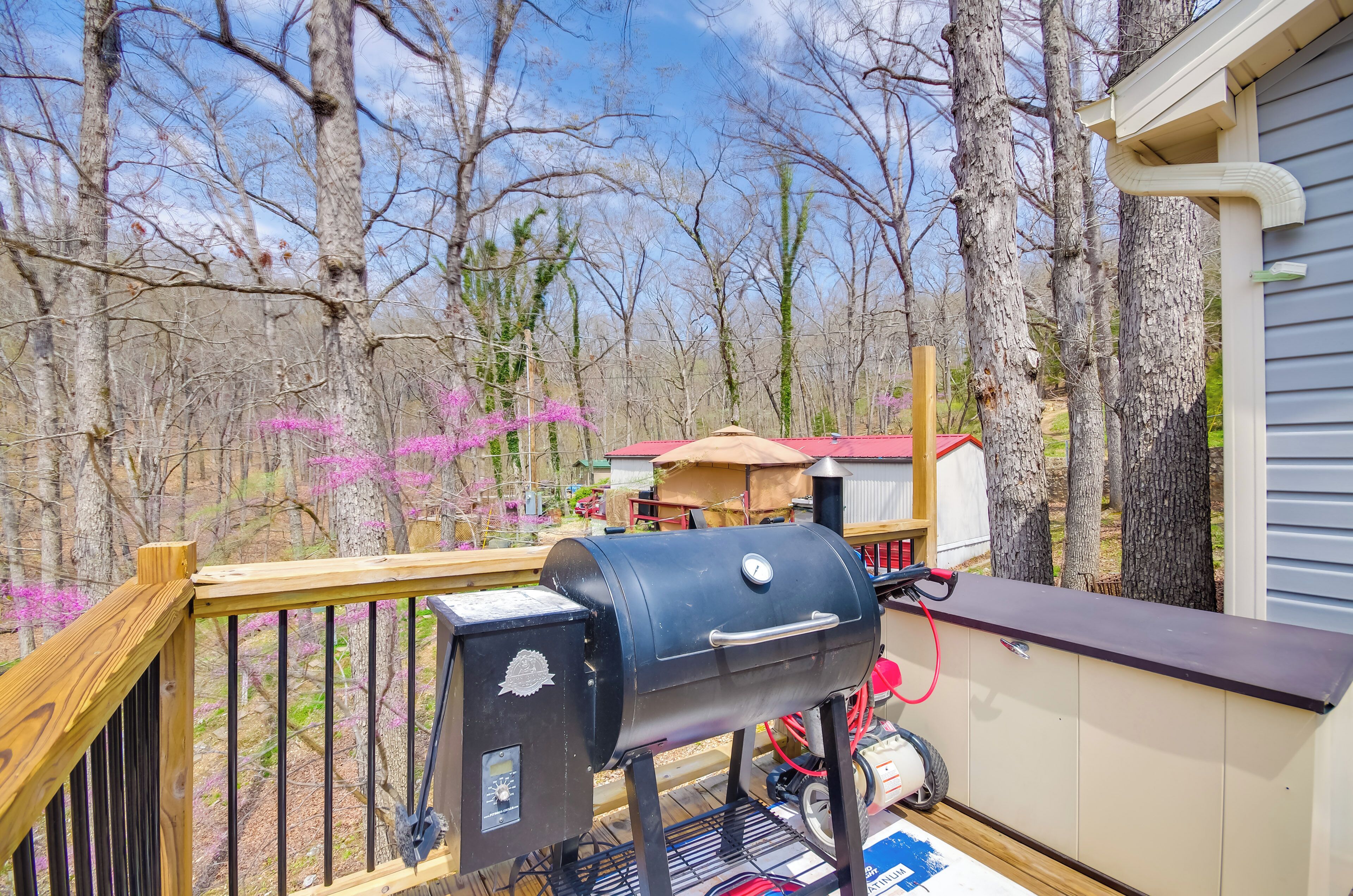 Eine Holzterrasse mit Grill, umgeben von Bäumen und einem Haus.