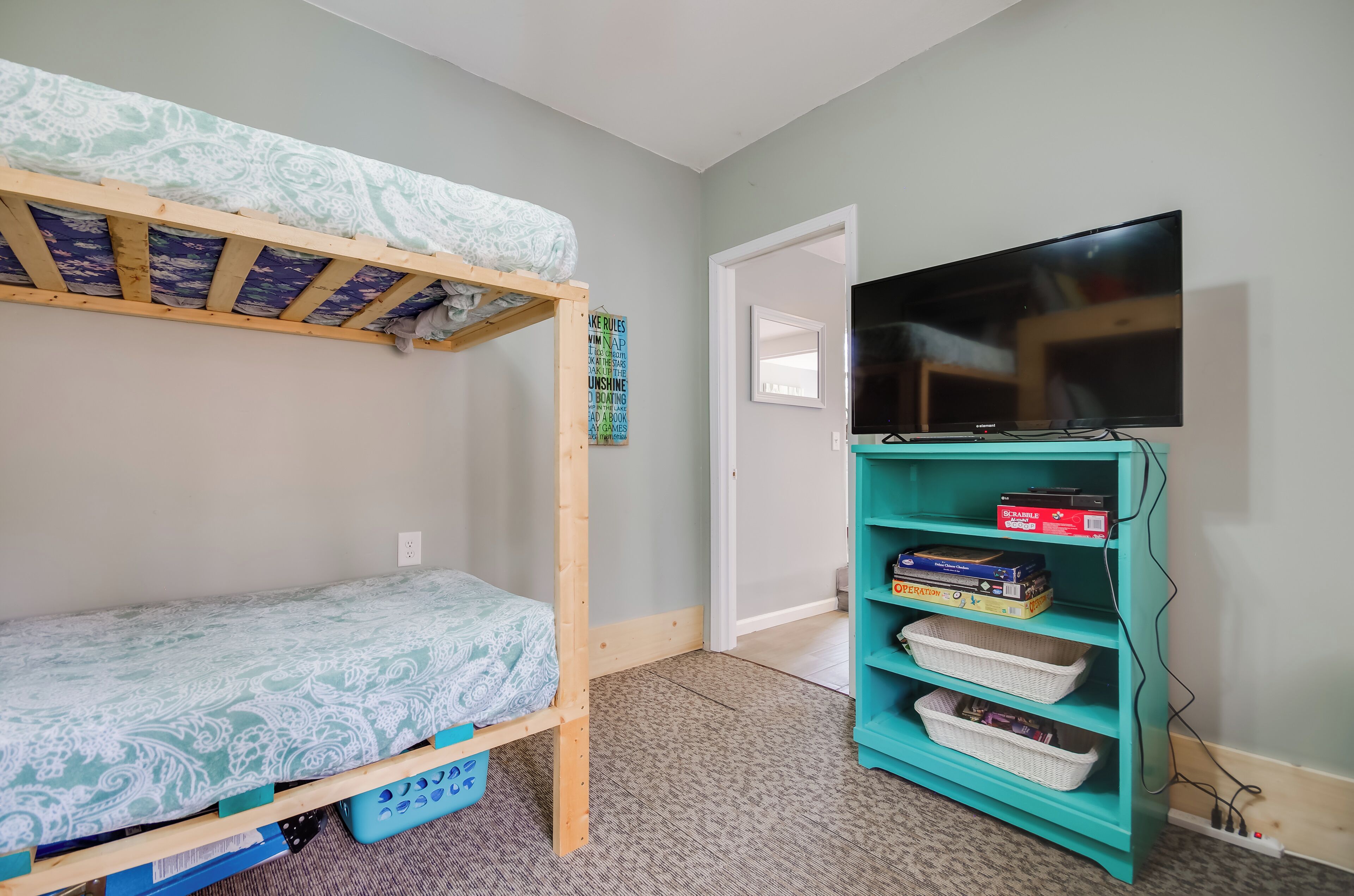 A bunk bed with patterned bedding, a teal bookshelf with board games, and a television on the wall.