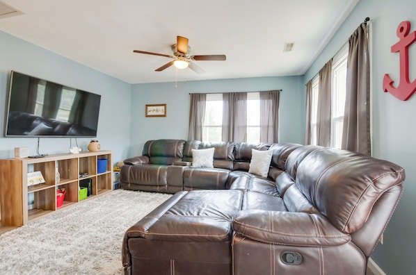 A living room with a sectional sofa, a ceiling fan, a flat-screen TV, and a wooden entertainment unit.