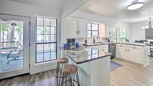 Une cuisine moderne avec des meubles blancs, un grand îlot central doté de tabourets et une vue sur l’extérieur grâce à de grandes fenêtres.
