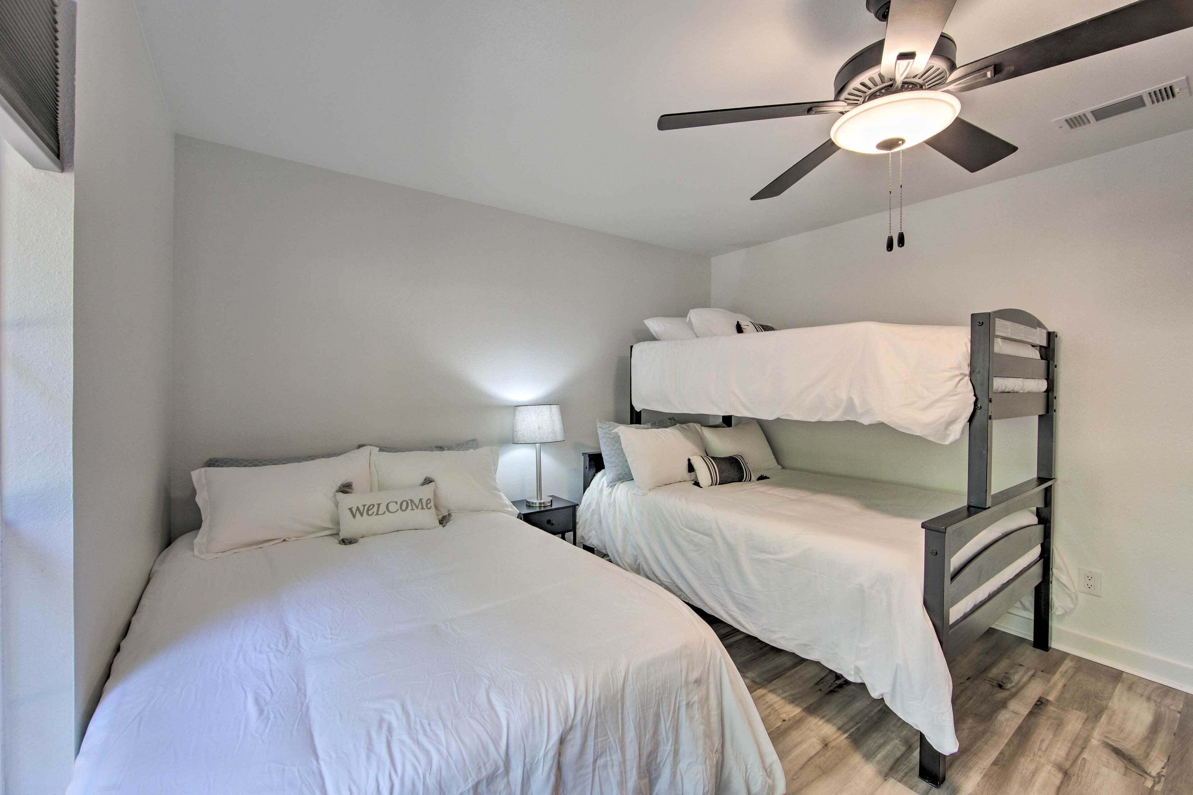 A bedroom with two single beds and a bunk bed, a ceiling fan, and a welcome sign.