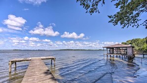 A wooden pier extending into calm water, a small wooden structure on stilts, and a distant shoreline with trees. - Luxe Lakehouse w/ Sunset Views on Lake Palestine! (Flint)