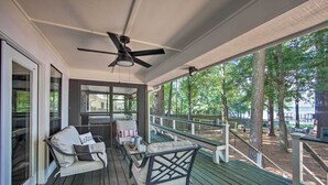 Une véranda couverte avec des sièges d’extérieur, un ventilateur de plafond et une vue sur les arbres environnants.