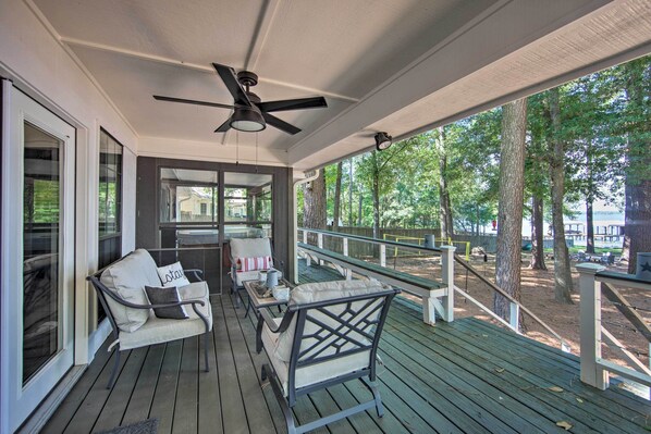 A covered porch with outdoor seating, a ceiling fan, and a view of the surrounding trees.