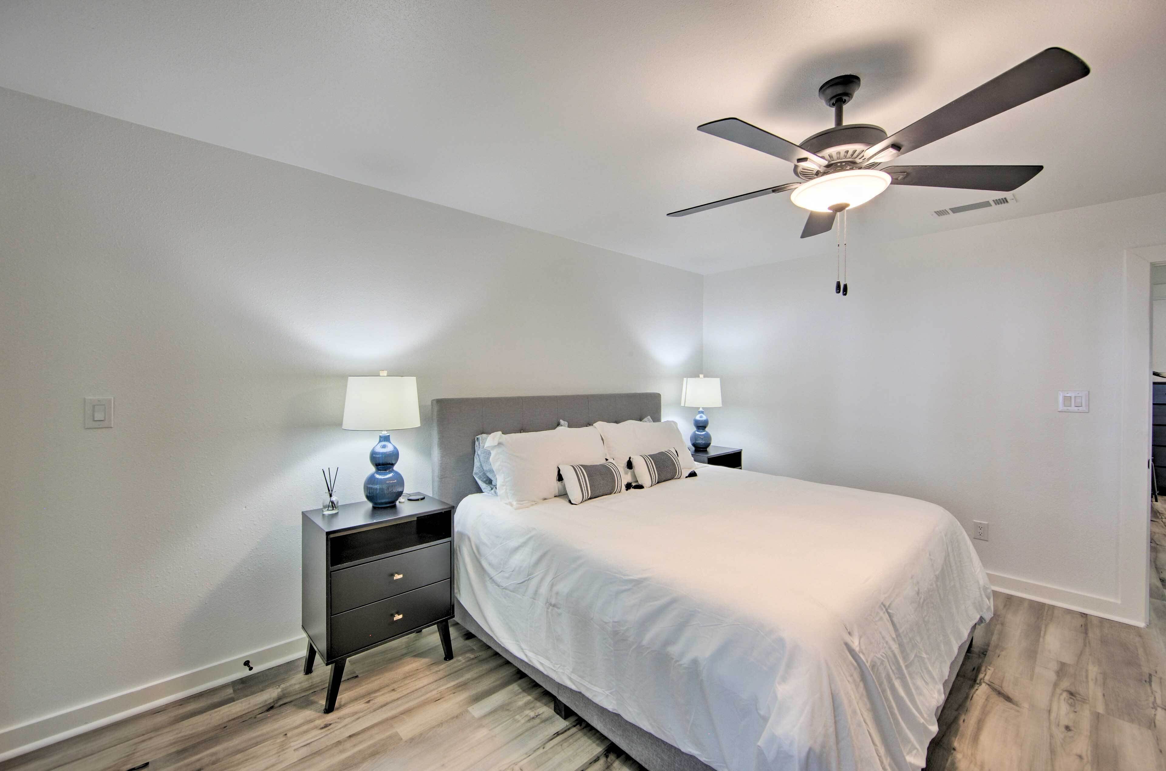 A bedroom with a bed, nightstands, a ceiling fan, and a door.