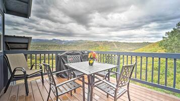 A wooden deck with a table and chairs, overlooking a hilly landscape.