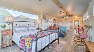 A bedroom with a bed, bedside lamps, a rocking chair, a small table, and a view of the mountains.