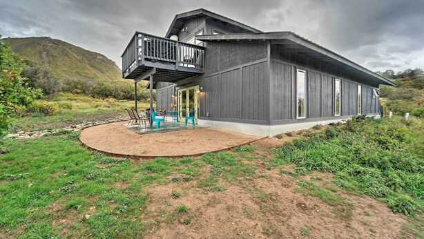 Una casa moderna con un balcone, un patio con sedie e vista su una collina.