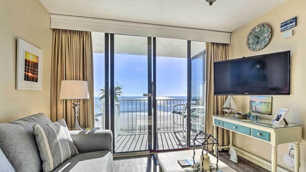 A hotel room with a balcony, a TV, a sofa, a desk, and a lamp. - Ocean Views & Pool Access: Myrtle Beach Condo! (Myrtle Beach)
