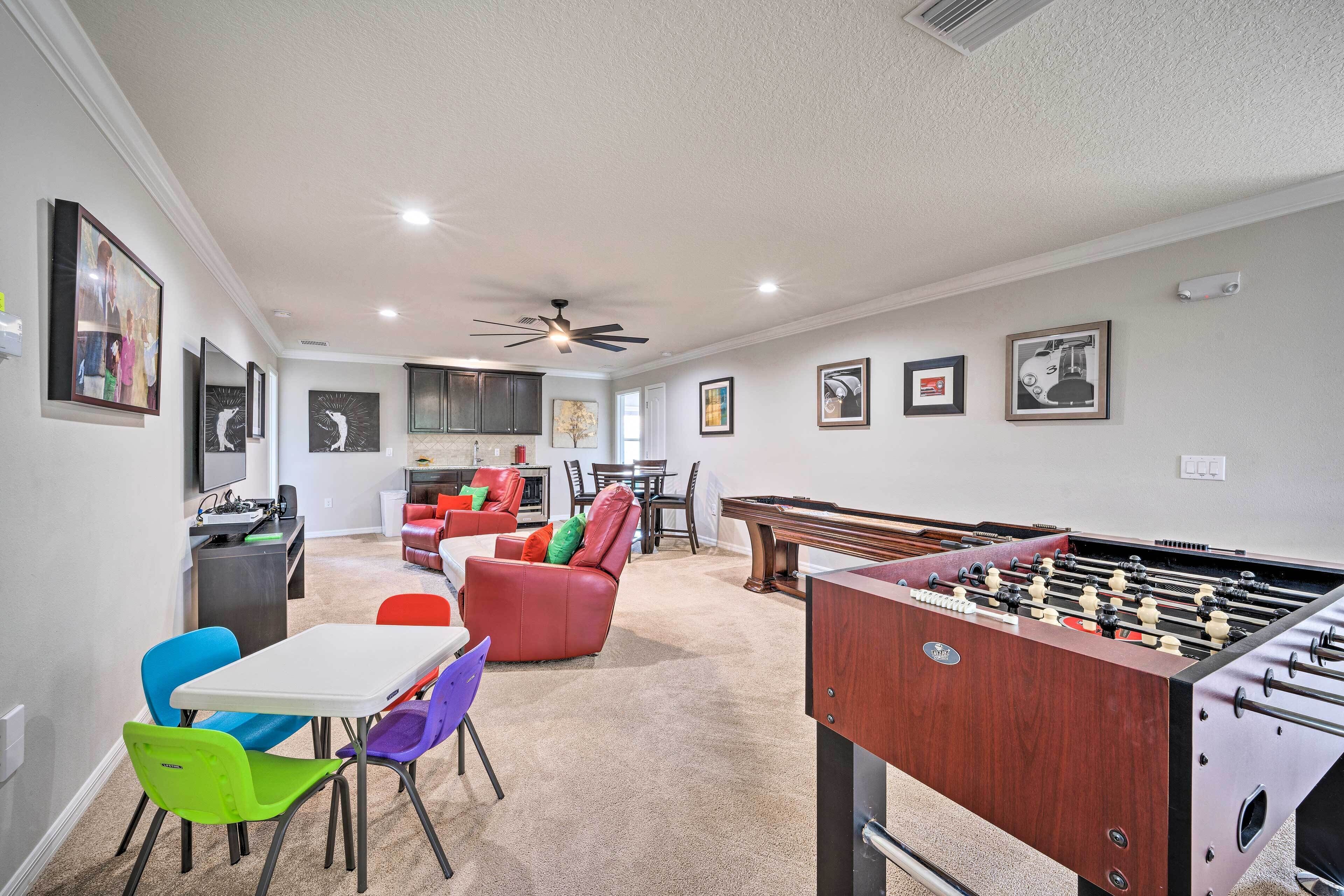 A spacious living area with a foosball table, colorful chairs, a kitchen, and a dining area.